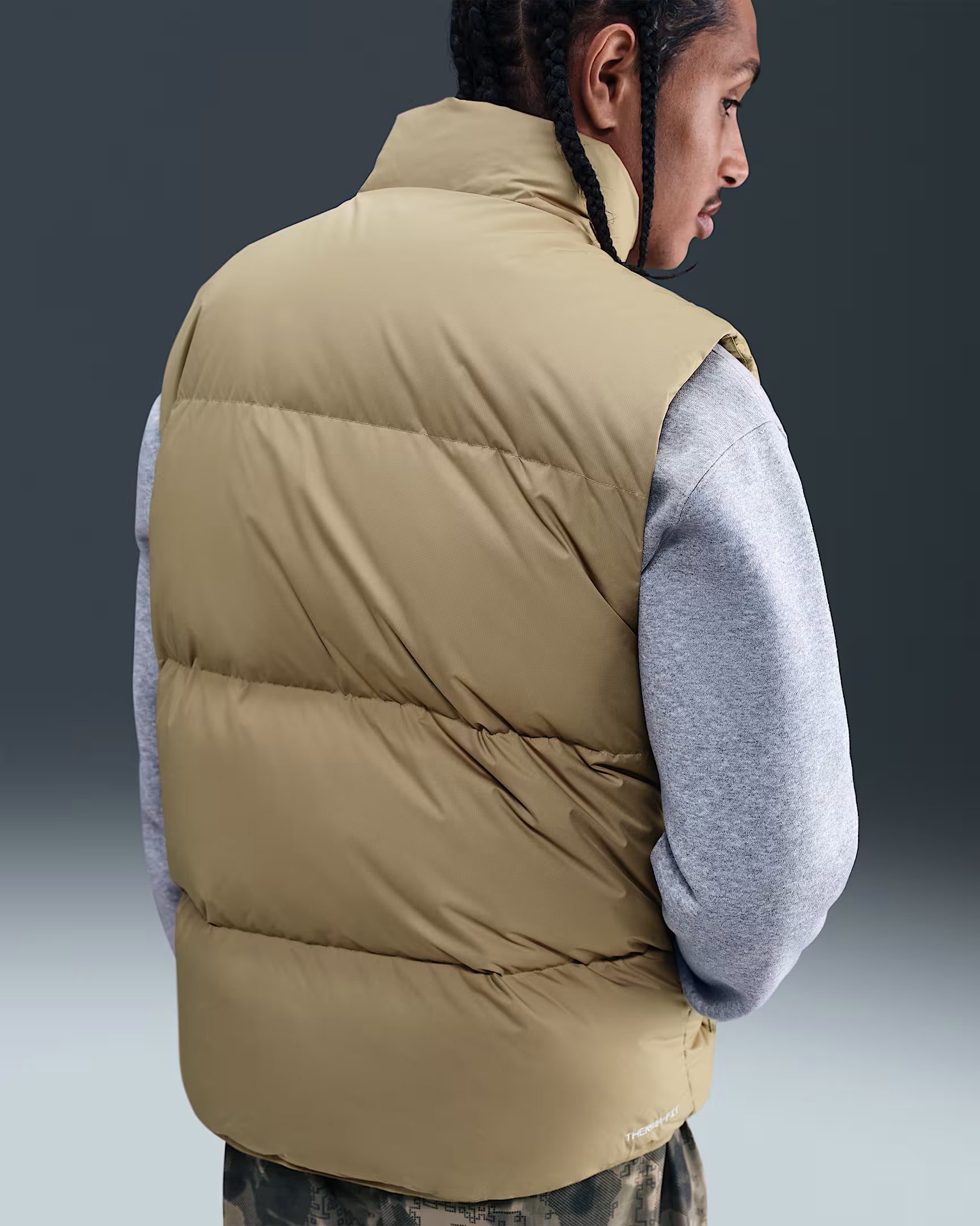Person wearing a beige puffer vest over a gray shirt on a gradient background