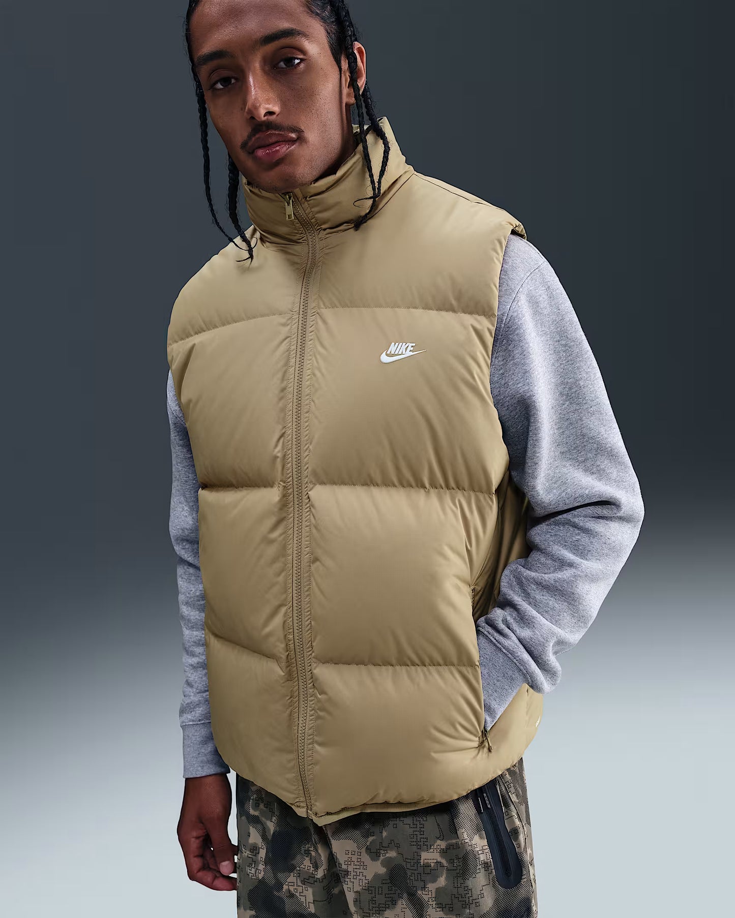 Person wearing a beige Nike puffer vest over a gray shirt with a dark background
